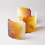 SILUETA ARCO TRIO AMBRA, a composition of three handcrafted sculptural candle objects in layered amber-toned pigments inspired by natural resin and golden light.