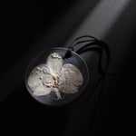 ESCLUSSO ORCHID NOCTURNE scented botanical wax sachet featuring a white orchid preserved in dark charcoal wax with black hanging cord.